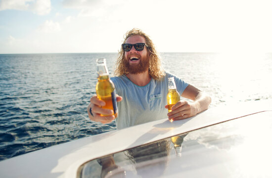 Bearded man on a boat handing out beers on a sunny day.
