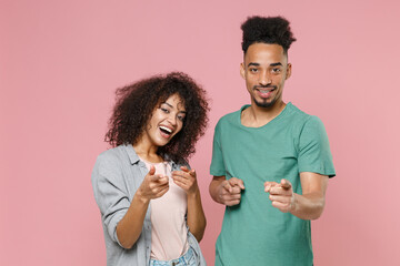 Cheerful smiling young african american couple friends guy girl in gray green casual clothes posing pointing index fingers on camera isolated on pastel pink color wall background studio portrait.