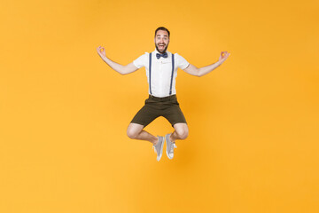 Full length portrait of excited young bearded man 20s wearing white shirt suspender shorts posing jumping hold hands in yoga gesture, relaxing meditating isolated on bright yellow background studio.