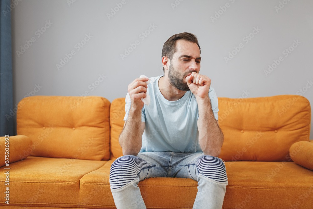 Wall mural sick tired exhausted young bearded man in casual blue t-shirt hold paper napkin coughing sneezing co