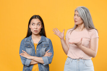 Puzzled displeased irritated family asian women girls mother and daughter in casual clothes posing holding hands crossed spreading hands swearing isolated on yellow color background studio portrait.