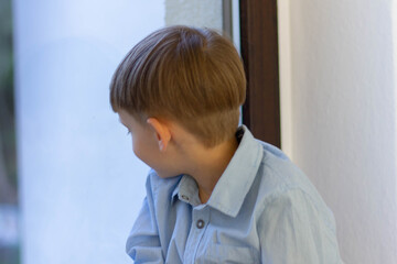 Little boy sits on the windowsill and looks out the window