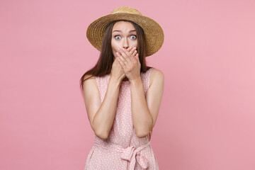 Shocked amazed surprised young brunette woman 20s wearing pink summer dotted dress hat posing covering mouth with hands looking camera isolated on pastel pink color wall background studio portrait.