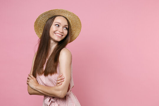 Smiling pretty attractive beautiful young brunette woman 20s wearing pink summer dotted dress hat posing holding hands crossed looking aside isolated on pastel pink wall background studio portrait.