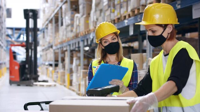 Young women workers with gloves and face mask working in warehouse.