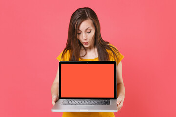 Naklejka premium Shocked amazed young brunette woman in yellow casual t-shirt posing hold looking on laptop pc computer with blank empty screen mock up copy space isolated on pink color background studio portrait.