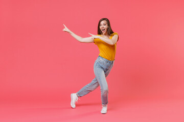 Full length portrait of excited young brunette woman 20s in yellow casual t-shirt pointing index fingers aside on mock up copy space keeping mouth open isolated on pink color wall background studio.