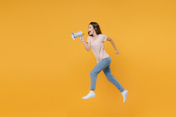 Fototapeta na wymiar Full length side view portrait of cheerful funny young woman 20s in pastel pink casual t-shirt posing jumping like running screaming in megaphone isolated on bright yellow color background studio.