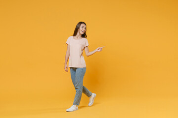 Full length portrait of cheerful smiling funny young woman 20s in pastel pink casual t-shirt posing pointing index finger aside on mock up copy space isolated on bright yellow color background studio.