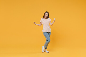 Fototapeta na wymiar Full length portrait of happy joyful young woman wearing pastel pink casual t-shirt posing clenching fists doing winner gesture keeping eyes closed isolated on yellow color wall background studio.