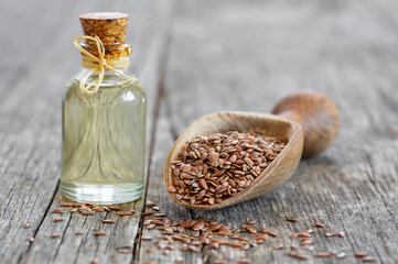 Heap of Flax seeds or linseeds in spoon or bowl with glass of flax seed oil on rustic backdrop....