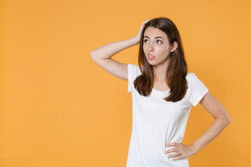 Obraz premium Preoccupied puzzled concerned young brunette woman 20s in white blank empty design casual t-shirt posing standing put hand on head looking aside up isolated on yellow color background studio portrait.