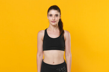 Fototapeta premium Beautiful attractive young fitness sporty woman 20s wearing black sportswear posing working out training standing and looking camera isolated on bright yellow color wall background studio portrait.