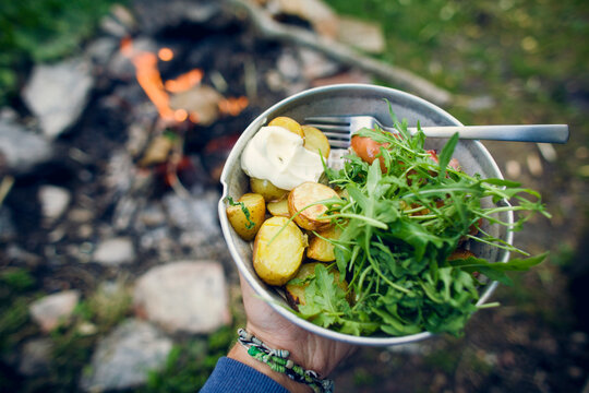 Person holding a plate with food next to a bonfire