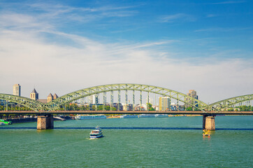 The Hohenzollern Bridge or Hohenzollernbrucke across Rhine river with tourist boat sailing on water, pedestrian and railway steel bridge, Cologne city centre, North Rhine-Westphalia, Germany