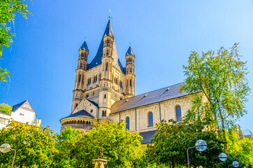 The Great Saint Martin Roman Catholic Church Romanesque architecture style building with spire on tower and green trees crown foreground, blue clear sky in summer day, North Rhine-Westphalia, Germany