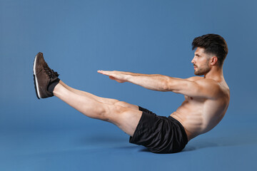 Full length portrait side view young fitness sporty strong guy bare-chested sportsman isolated on blue background. Workout sport motivation lifestyle concept. Doing abdominal exercises looking aside.