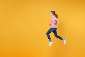 Fototapeta na wymiar Full length children studio portrait side view of smiling little ginger redhead kid girl 12-13 years old wearing pink casual t-shirt posing jumping like running isolated on yellow color background.