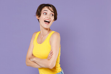 Side view of excited young brunette woman girl in yellow casual tank top posing isolated on pastel violet background studio portrait. People lifestyle concept. Holding hands crossed, looking aside.