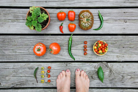 Looking down on a woman's feet surrounded by a garden harvest on a wooden background.