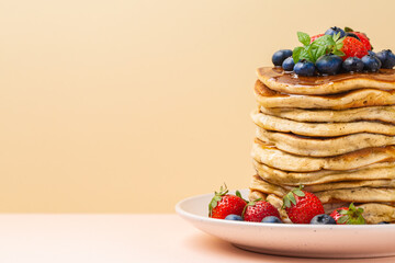 Pancakes with honey, strawberries and blueberries. Copy space, text box. Peach and pink background. Close up.