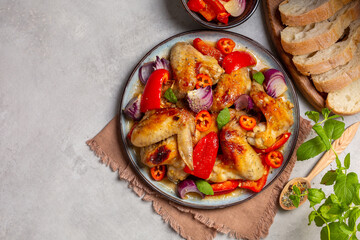 A dish of baked chicken wings marinated in orange jam, with bell peppers, hot peppers and red onions. Copy space.