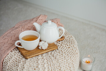 A mug of hot tea, a teapot, a wooden stand on an ottoman. Cozy autumn. Winter breakfast. Cotton.