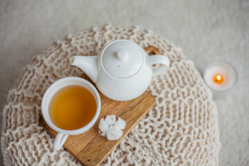 A mug of hot tea, a teapot, a wooden stand on an ottoman. Cozy autumn. Winter breakfast. Roses. Candle.