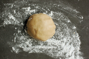 Ginger cookie dough on floured black surface. View from above. The dough has a brown tint. Cooking ginger biscuits. Christmas atmosphere. Ball of dough. Copy space for text, Homemade pastries. Holiday