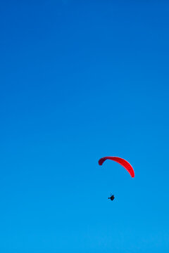 Image of the silhouette of a man paragliding against a bright blue sky