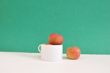 Apples in a white cup with an isolated apple giving the concept of separation on green background and white base