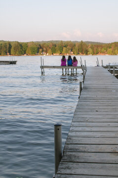 three young women sit at the end of a dock