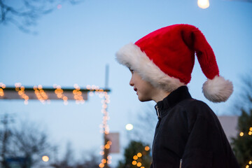 Happy boy wearing Santa hat at Christmas tree stand