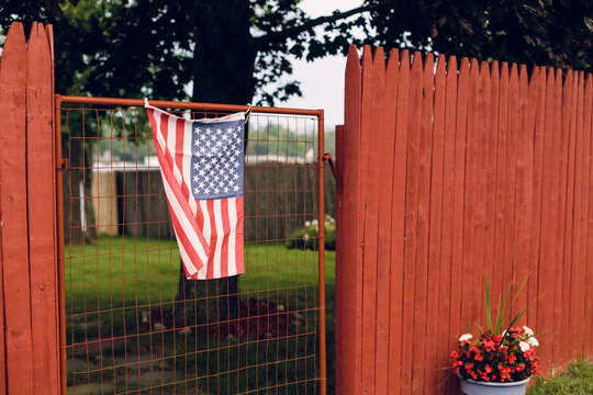 An Amerian flag hangs on an old gate between a red fence.