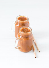 Yellow plum smoothie in a glass jar with a bamboo straw on a light background