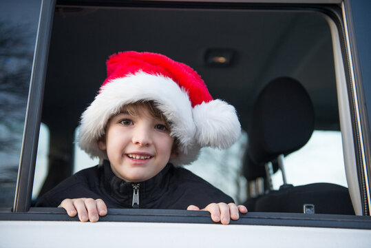 Cute boy wearing Santa Claus hat peeks out the window of the car