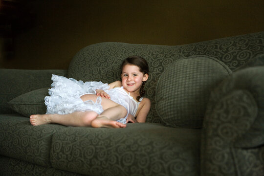 Little girl in white slip dress relaxing on green couch