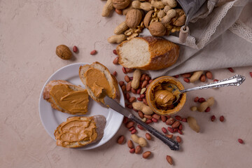 Peanut butter in a jar with bread on a white plate, peanut butter sandwich, nuts scattered on the table. walnuts. Still life, healthy food concept. Allergens