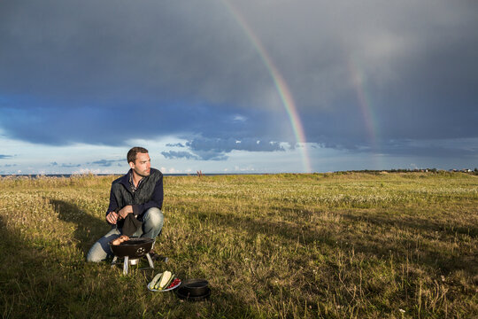 Man barbecuing with rainbow in the background