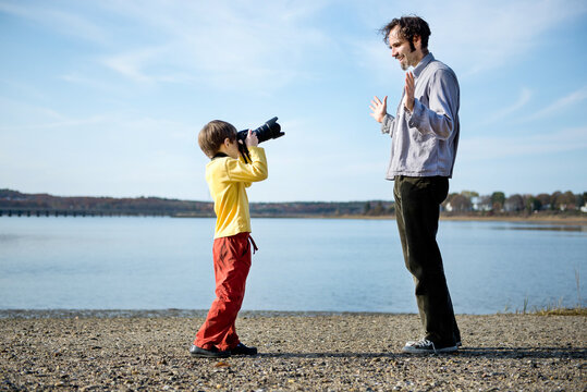 Boy on a beach takes a picture of his father with a digital SLR camera
