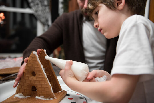 Boy and his father build a gingerbread house together
