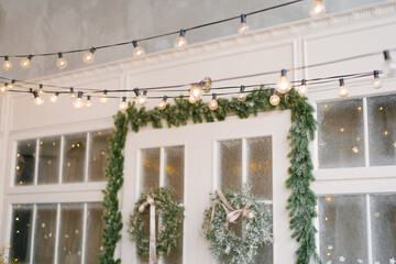 A retro garland of incandescent lamps is lit against the background of the entrance doors to the house, decorated with Christmas wreaths