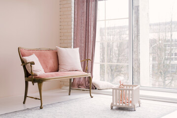 A pink vintage sofa with pillows stands near the window in the living room or children's room in...