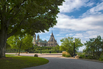 View of Canadian Parliament from Major's Hill Park under blue cloudy skies with long sweeping walkways, lawns, trees and lampposts in foreground nobody