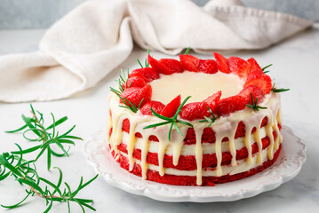 Homemade red velvet cake with white chocolate,  fresh strawberries and rosemary. Delicious gourmet dessert in a white plate on a marble surface close-up. Selective focus, copy space
