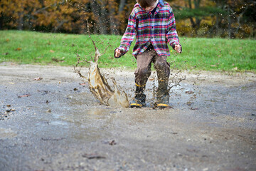 Boy wearing rubber boots splashes in a mud puddle