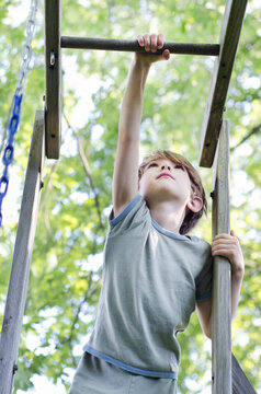 Child Reaches High To Reach The Monkey Bars Of His Backyard Playset