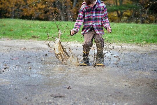 Boy wearing rubber boots splashes in a mud puddle