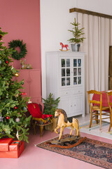 Vintage living room decorated for Christmas and New Year. Wooden rocking horse toy near the Christmas tree with gifts