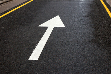 Arrow sign on the road. White arrow on the asphalt. White forward arrow on a blurry street background